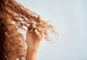 Image of a girl's hair with her fingers running through the frizzy hair. Taken from Unsplash