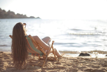 A woman sits on the beach with her hair draped over the back of a beach chair. Credit: Andrea Piacquadio, Pexels.