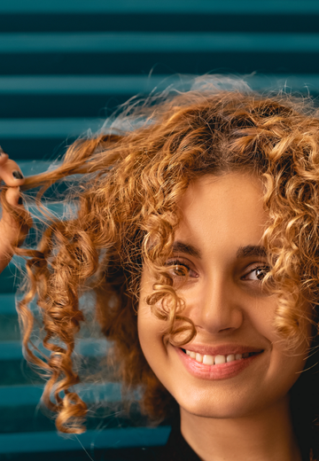 Image of a girl with curly hair smiling at the camera. Taken from Unsplash.