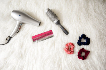 Image of a hairbrush, hairdryer, comb and hair bobbles on a fur surface. Taken from Pexels