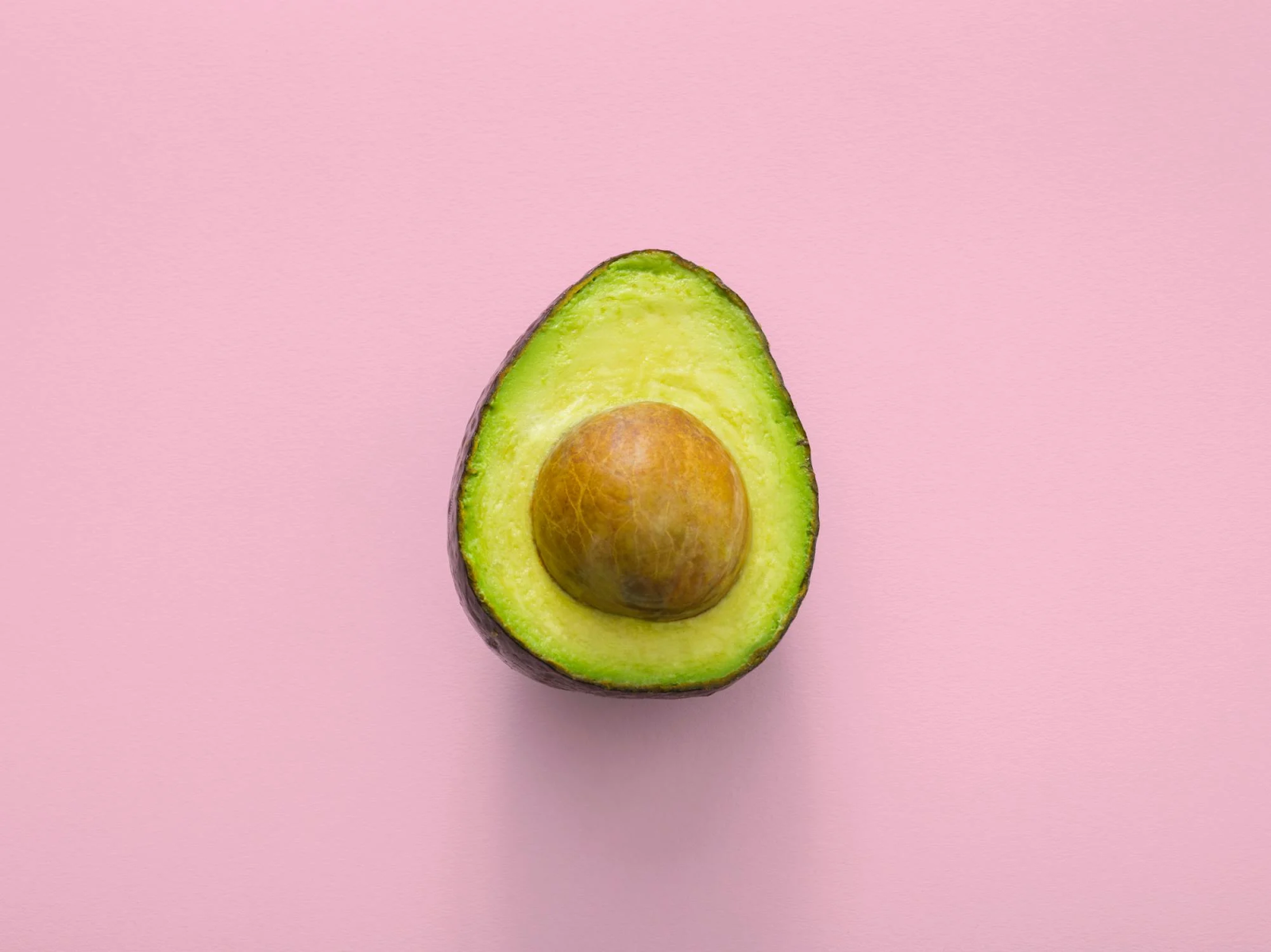 A sliced avocado with the inside facing upwards, offset with a pink background.