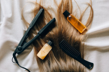 Straightened hair laid out on a bed and overlaid with hair styling products and tools.