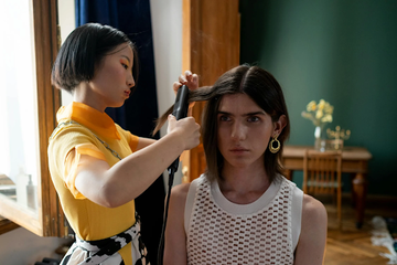 A woman looking in the mirror, having her hair curled with a straightener.