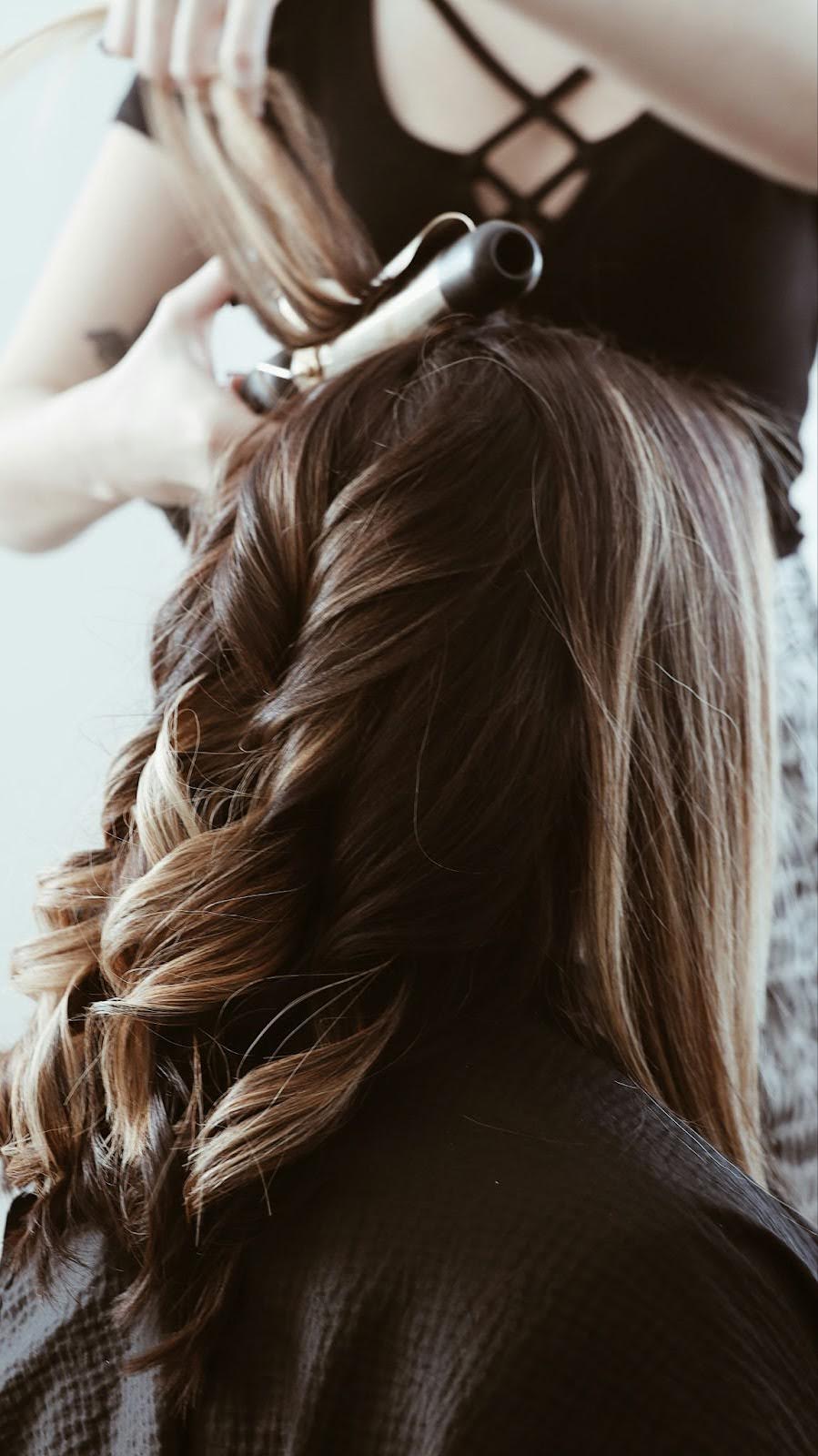 A girl with medium-length brown hair gets her hair curled by another female. Source: iStock.