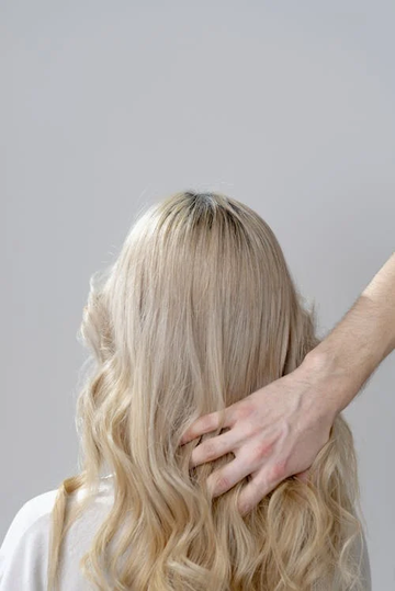 A hand brushing the back of a woman’s medium-length curled beach blonde hair. Source: Pexels