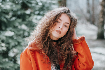 A woman standing in a forest, scrunching her brunette, naturally curly hair.