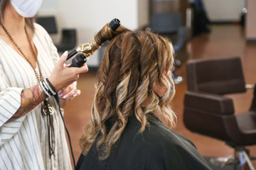 A woman in a salon having her permed hair curled by a stylist.