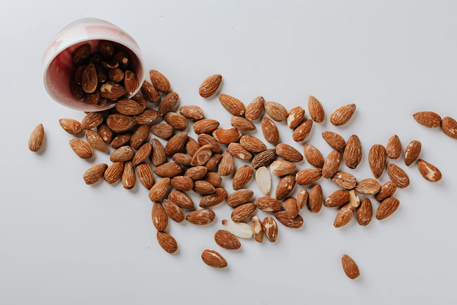 A bowl containing almonds tipped over and the almonds scattered everywhere.