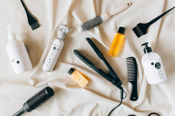 Image of hair tools and hair products on a white bedspread. Taken from Pexels