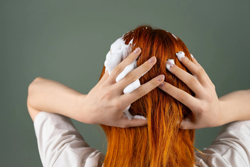 A woman with bright orange hair massaging shampoo into her strands.