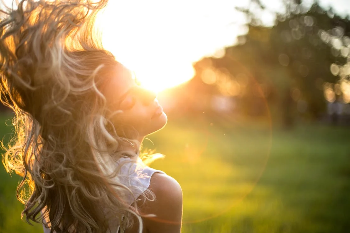 A blonde woman swishing her beachy hair in the wind on a sunny day.