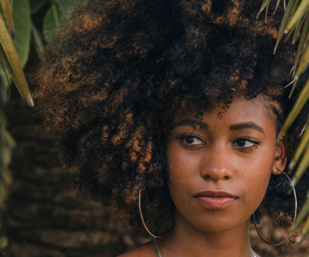 Dark-skinned woman glancing in front of her at a side angle with her 4c style curls parted in one direction.